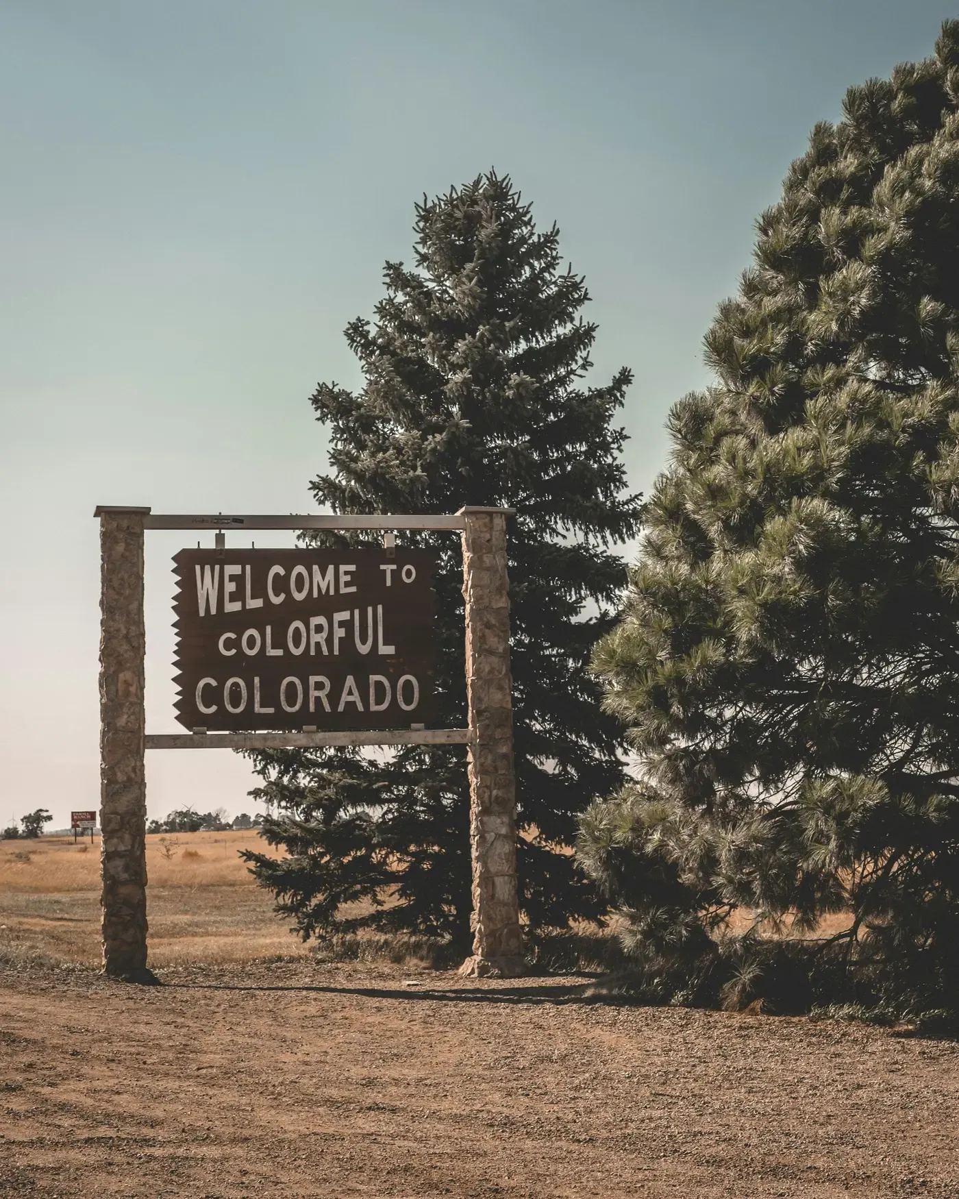 Roadside sign reading Welcome to Colorful Colorado beside evergreen trees