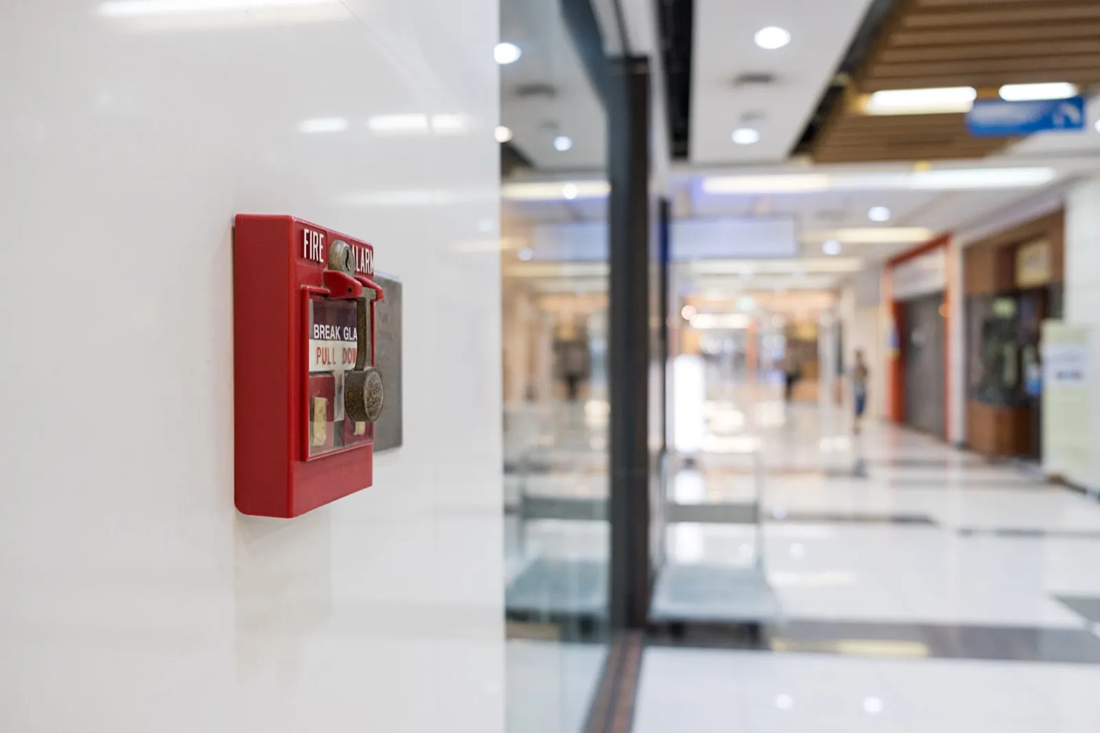 A red fire alarm pull station reading "break glass, pull down" mounted on a wall in a commercial corridor